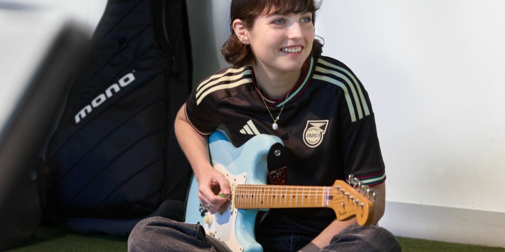 A young person sitting on the ground playing the guitar