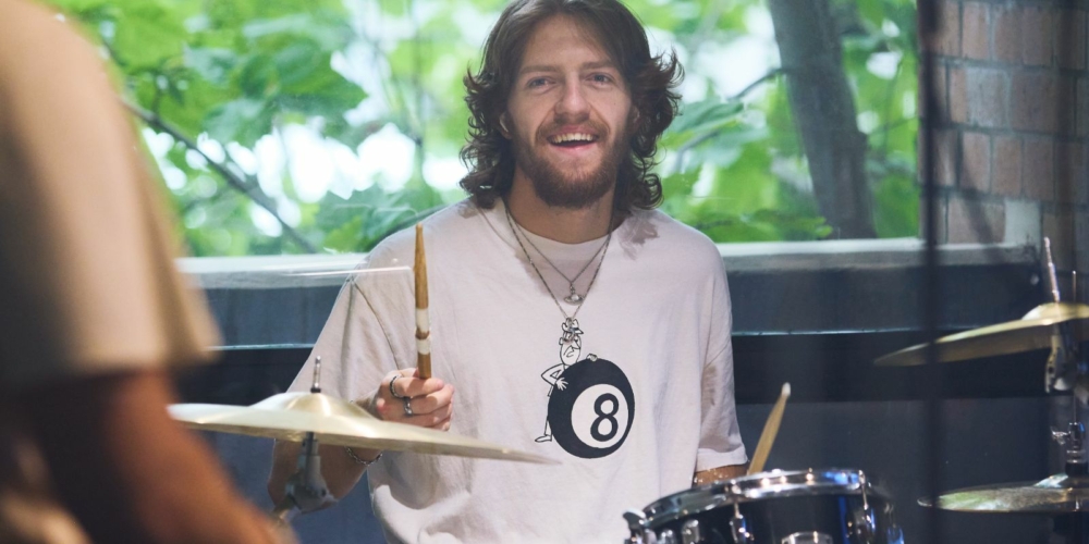 A person sitting playing the drums and smiling