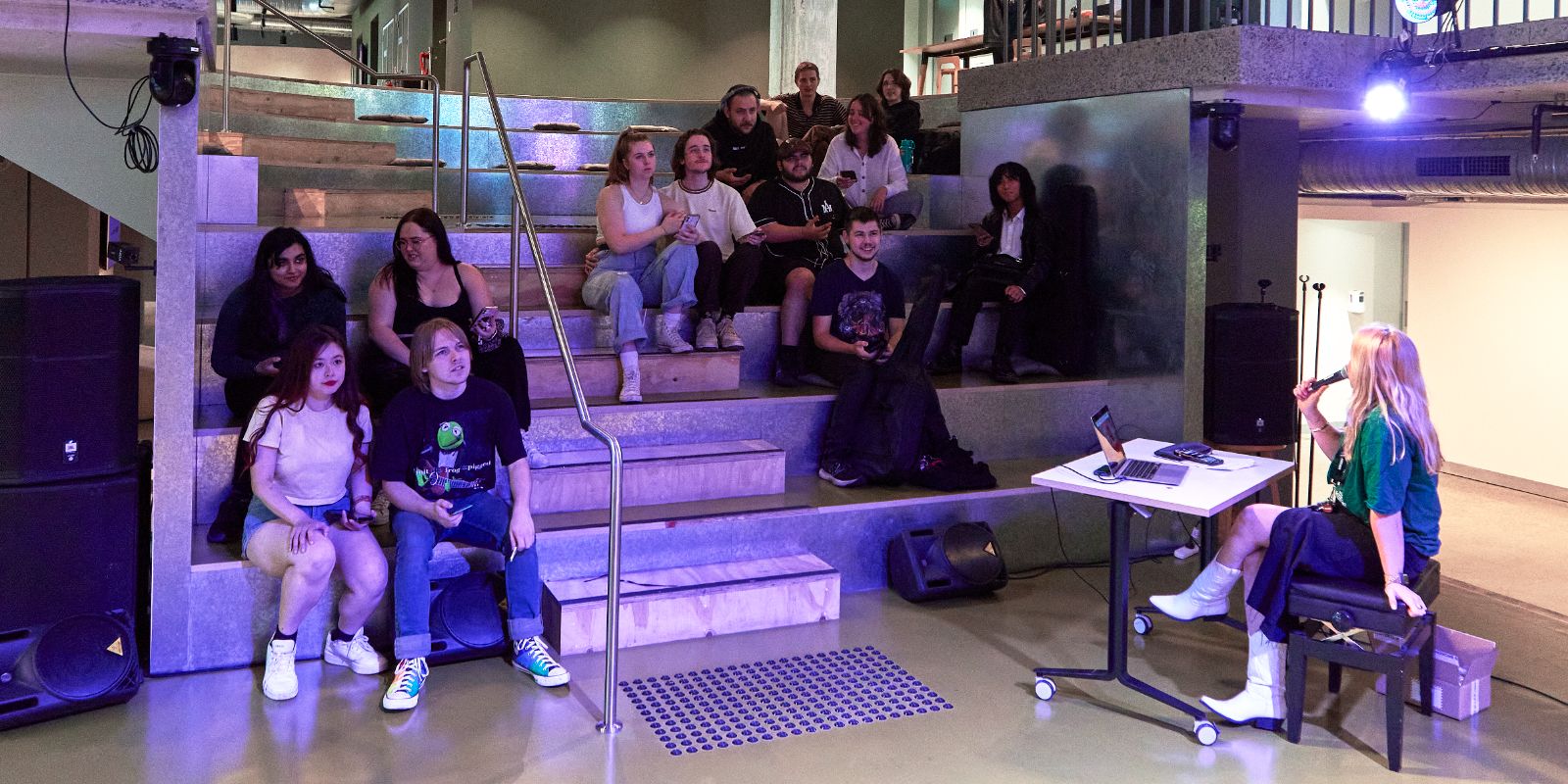 Student audience in an amphitheatre with a host on stage.