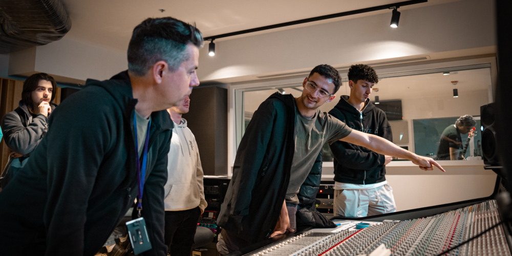 Three men standing over a music mixing console.