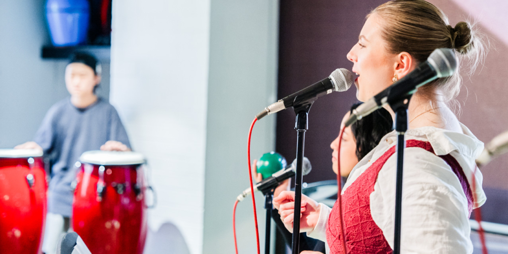 A male student playing congo drums next to a female student singing.