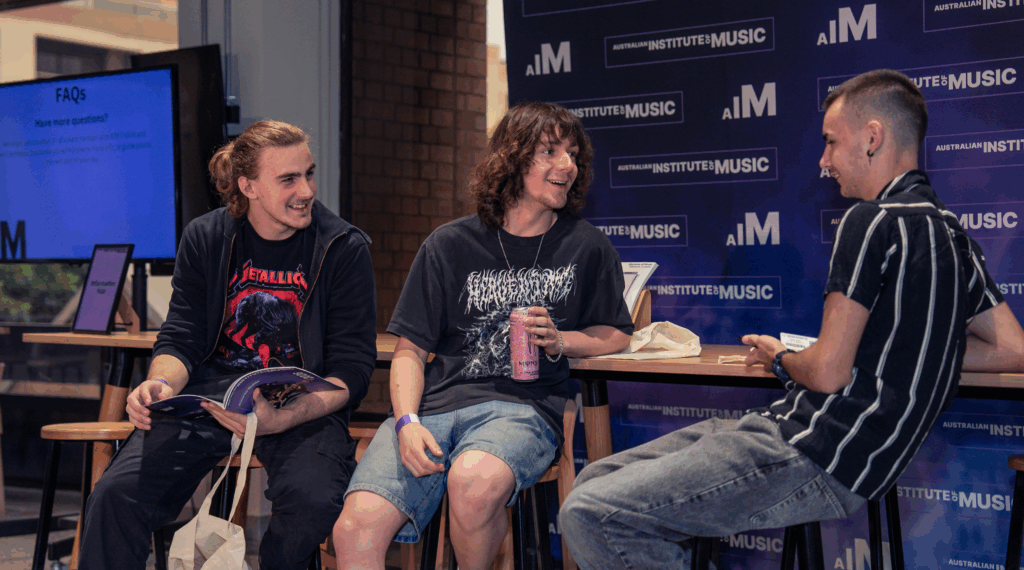 Three male students sitting in front of a Australian Institute of Music banner. 